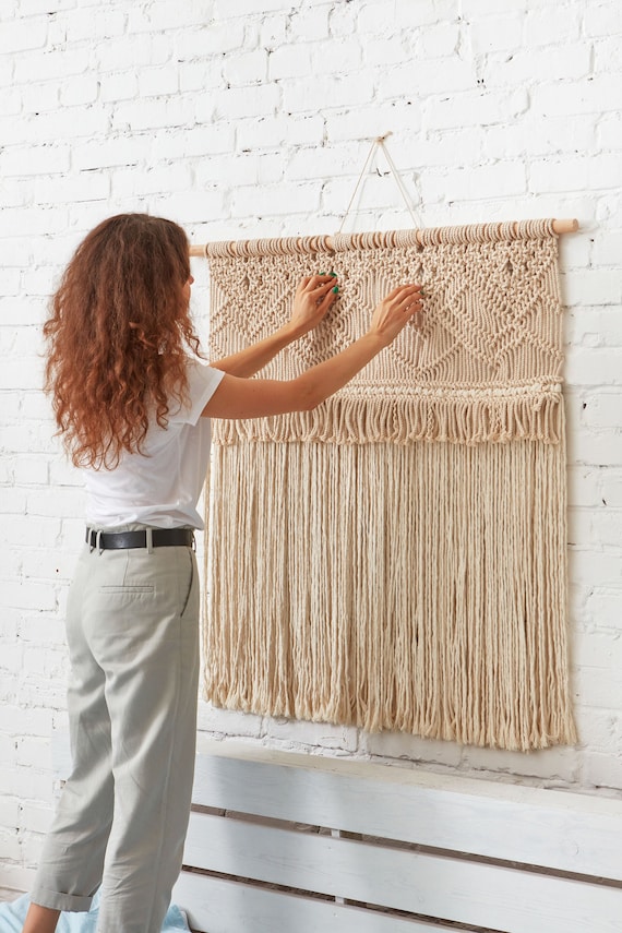Large woven macrame tapestry hanging on a white wall