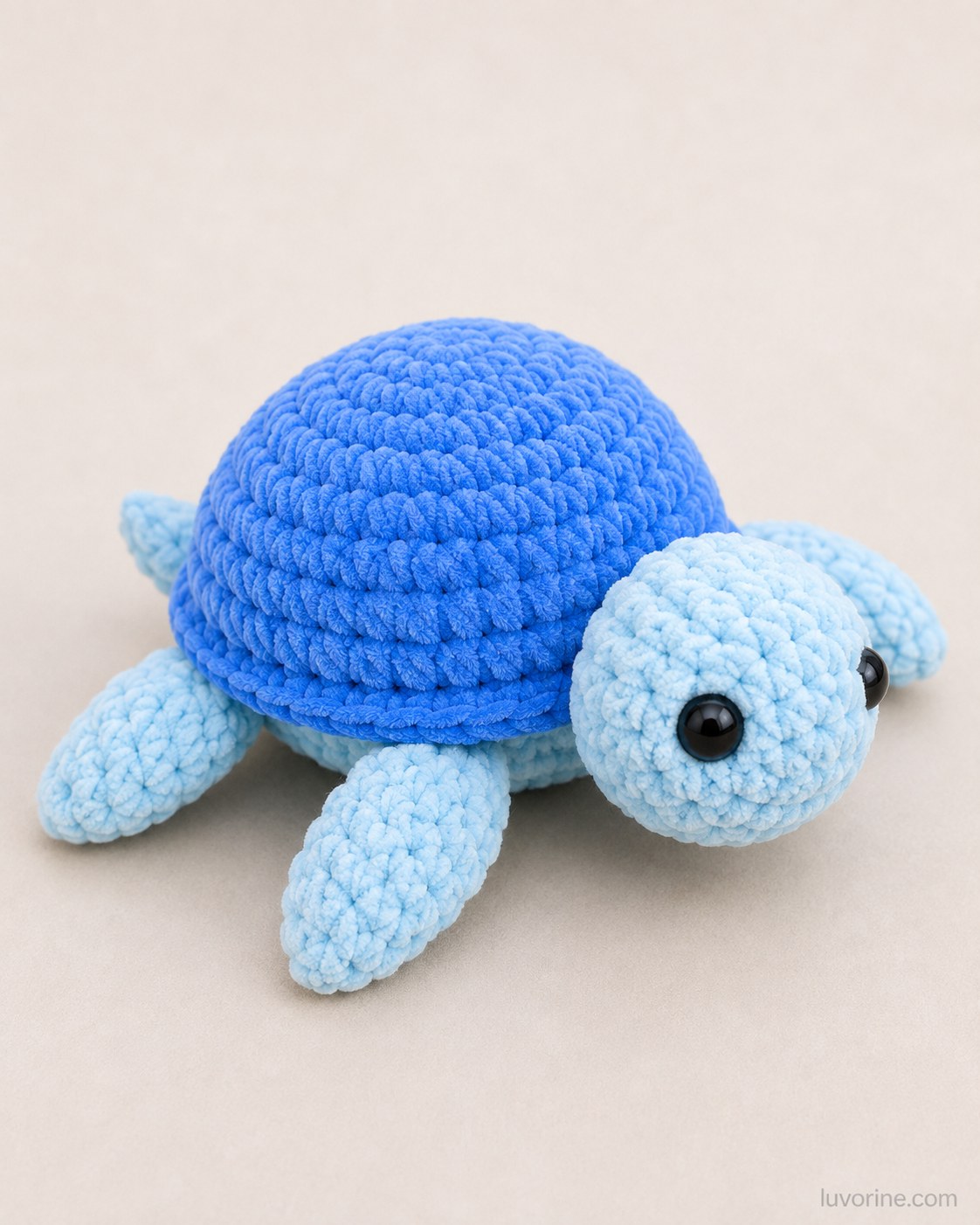 The finished blue no-sew plush turtle sitting on a plain background after crocheting